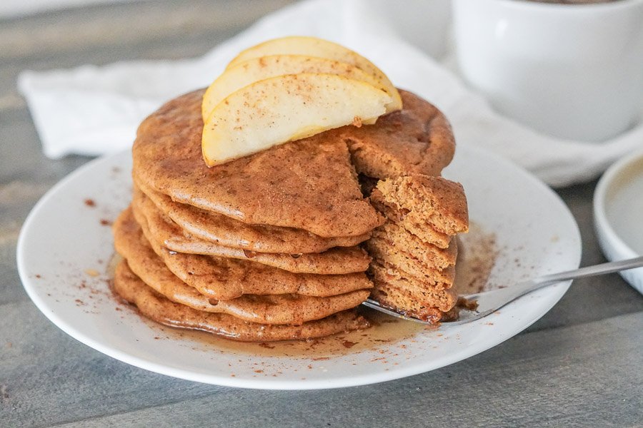 Side view of a tall stack of paleo pumpkin pancakes with a tall bite on a fork to show the super fluffy texture!
